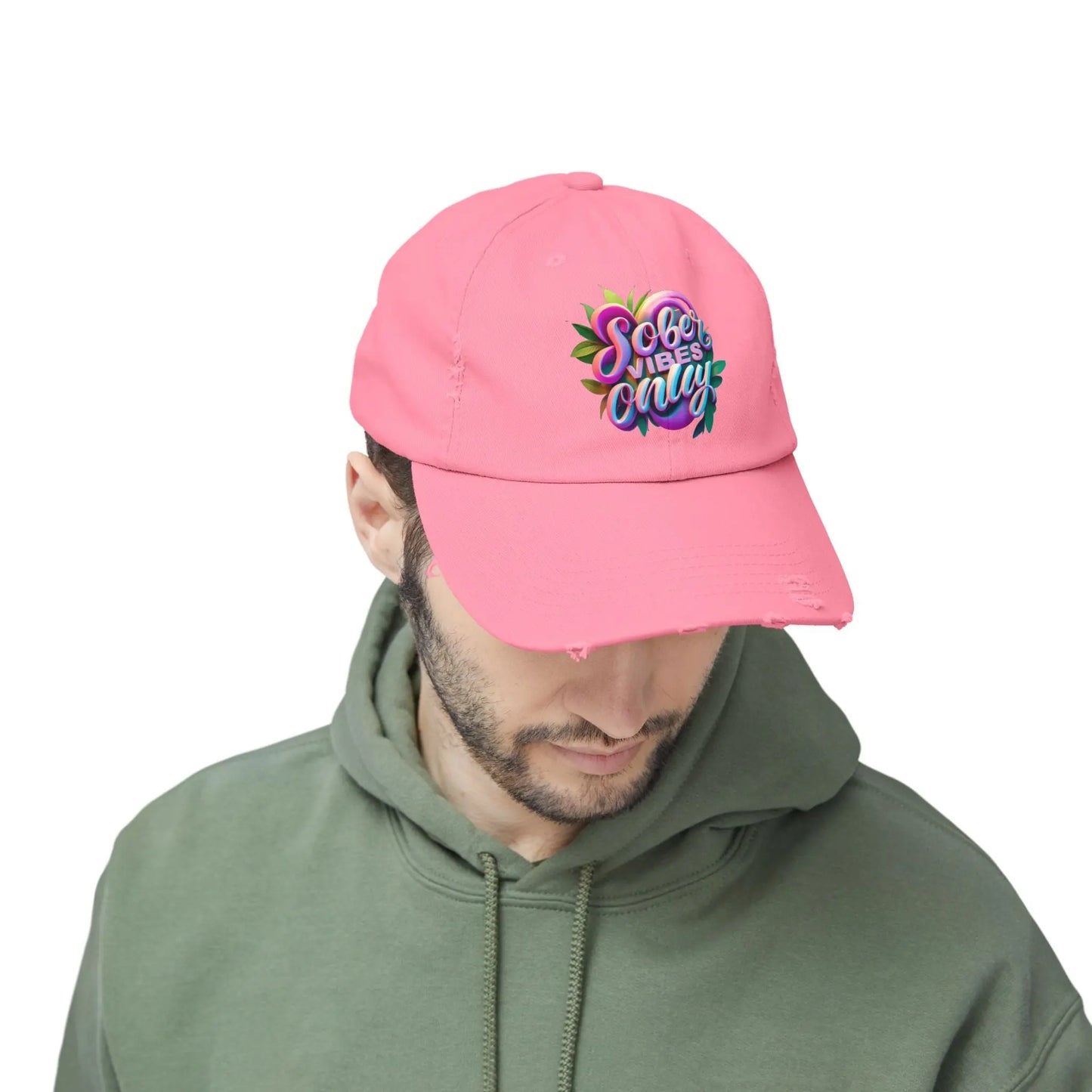 Person wearing a pink cap with colorful text and a green hoodie on a white background